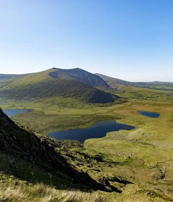 Rolling green hills and a mountain under a clear blue sky, with small lakes nestled in the grassy valley below.